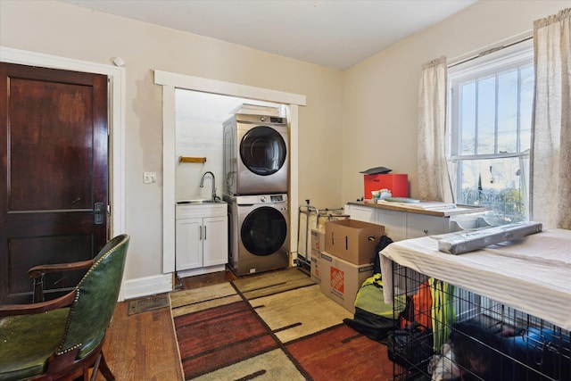clothes washing area featuring stacked washer and clothes dryer, cabinet space, light wood-style flooring, and a sink