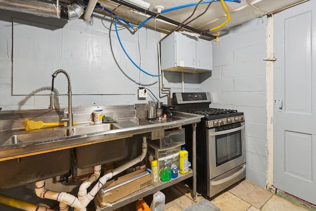 kitchen with stainless steel range with gas cooktop, white cabinetry, concrete block wall, and a sink