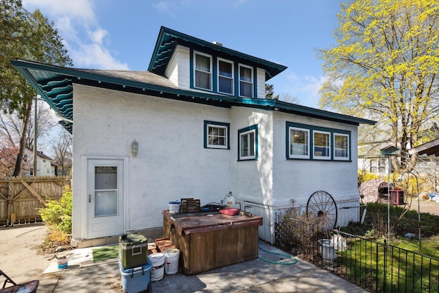 rear view of property featuring fence, a patio area, stucco siding, and a hot tub