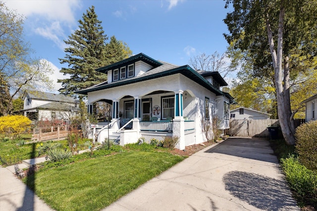 bungalow featuring a front lawn, covered porch, driveway, stucco siding, and fence