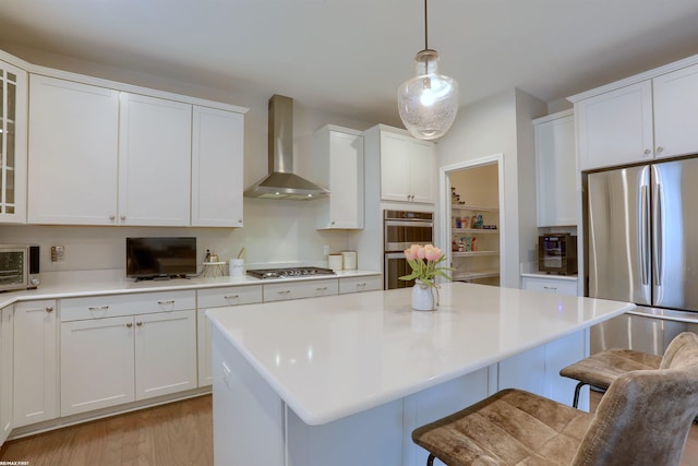 kitchen with wall chimney exhaust hood, a breakfast bar, white cabinets, and appliances with stainless steel finishes