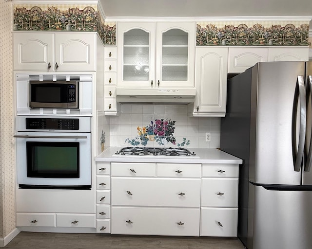 kitchen with stainless steel appliances, under cabinet range hood, tasteful backsplash, light countertops, and white cabinets