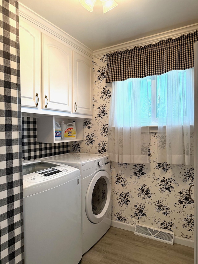 washroom featuring independent washer and dryer, visible vents, wallpapered walls, cabinet space, and wood finished floors