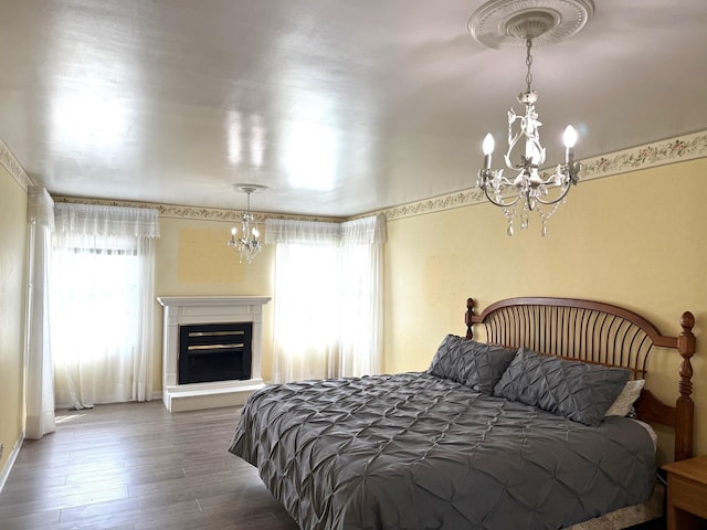 bedroom with a chandelier, wood finished floors, and a glass covered fireplace