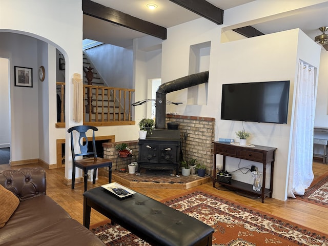 living room featuring a wood stove, stairway, arched walkways, beam ceiling, and wood finished floors