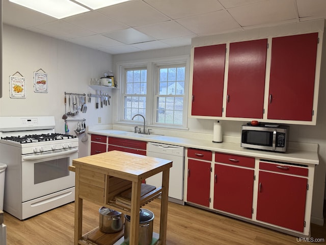 kitchen featuring red cabinets, a sink, light countertops, a drop ceiling, and white appliances
