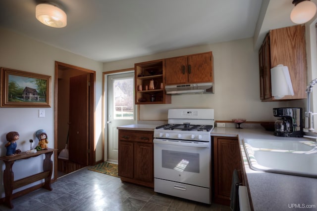 kitchen featuring brown cabinets, open shelves, light countertops, under cabinet range hood, and gas range gas stove