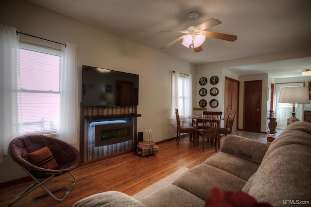 living room with ceiling fan, visible vents, baseboards, a glass covered fireplace, and wood finished floors