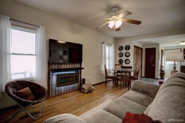 living area with ceiling fan, baseboards, wood finished floors, and a glass covered fireplace