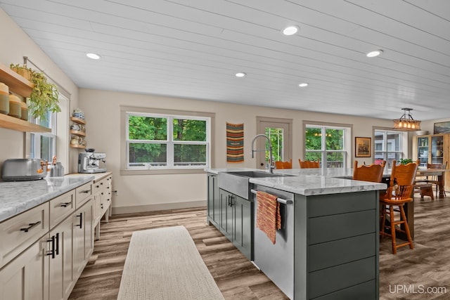 kitchen featuring stainless steel dishwasher, open shelves, a sink, light stone countertops, and a kitchen island with sink