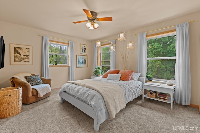 bedroom featuring carpet flooring, multiple windows, and ceiling fan with notable chandelier