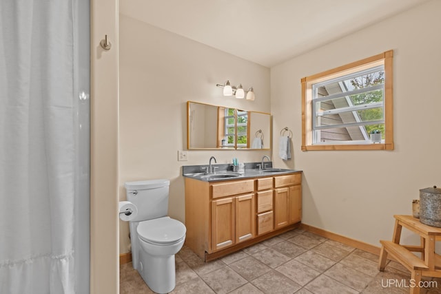 full bathroom with baseboards, toilet, double vanity, and a sink