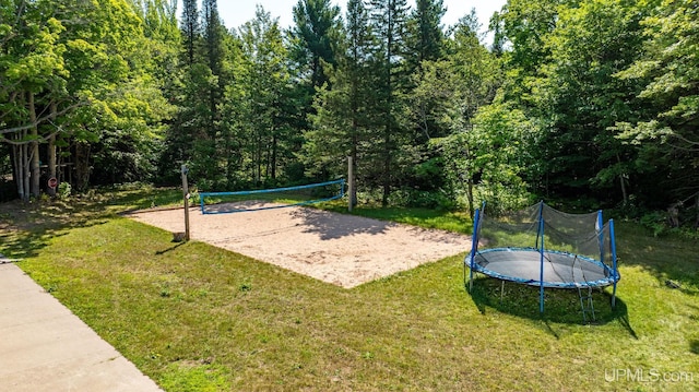 view of community featuring a wooded view, a trampoline, volleyball court, and a yard