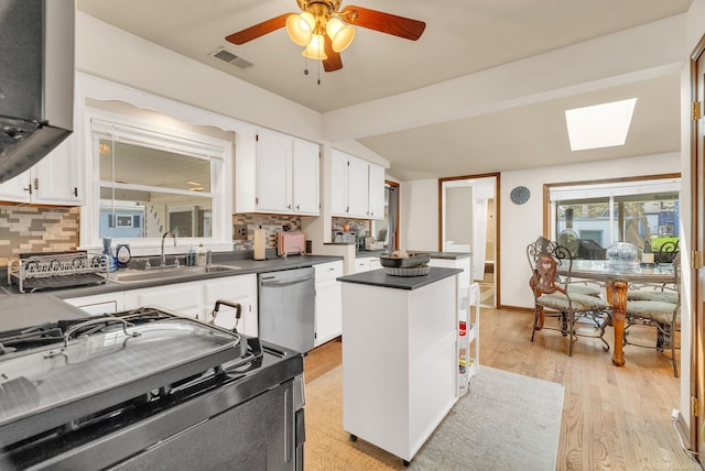 kitchen with stainless steel dishwasher, range, dark countertops, a sink, and visible vents