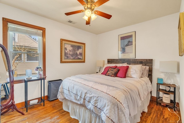 bedroom with wood finished floors, visible vents, ceiling fan, and baseboards