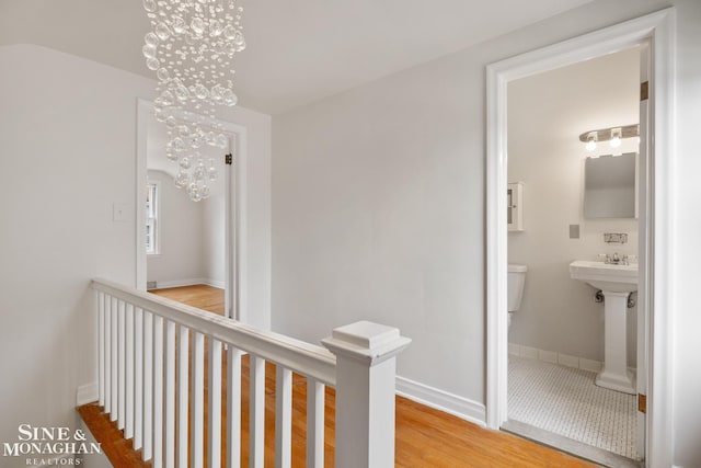 hallway featuring an upstairs landing, a notable chandelier, wood finished floors, and baseboards