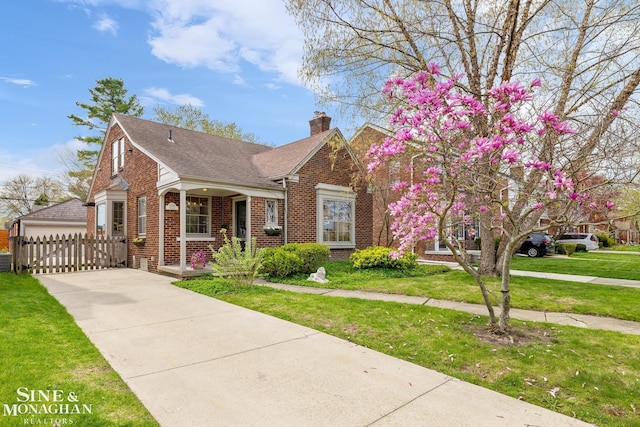 bungalow-style home featuring a chimney, a shingled roof, a front yard, fence, and brick siding