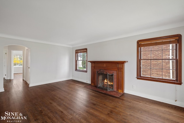 unfurnished living room with a fireplace, baseboards, dark wood-style floors, and arched walkways