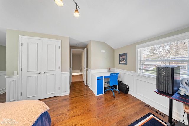 bedroom with visible vents, vaulted ceiling, wood finished floors, a wainscoted wall, and a closet