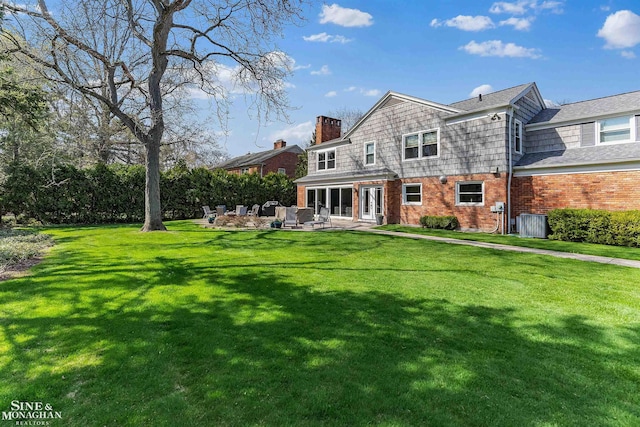 rear view of house with a patio, a chimney, a yard, and brick siding