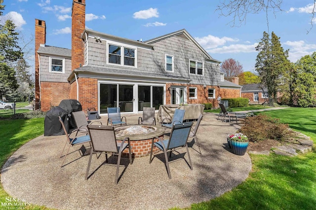 rear view of house featuring a chimney, a lawn, brick siding, a patio, and a fire pit
