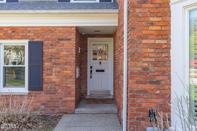 entrance to property featuring a shingled roof and brick siding