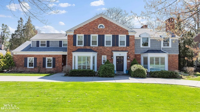 colonial house featuring brick siding, a chimney, and a front yard
