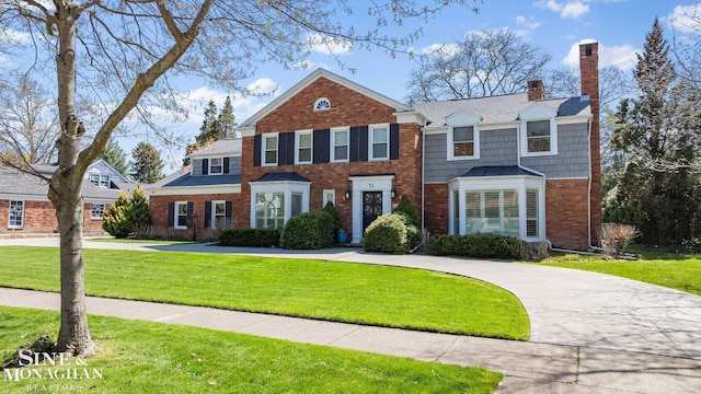 view of front facade with brick siding, a front yard, and a chimney