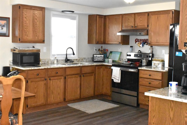 kitchen featuring brown cabinetry, a sink, under cabinet range hood, and black appliances