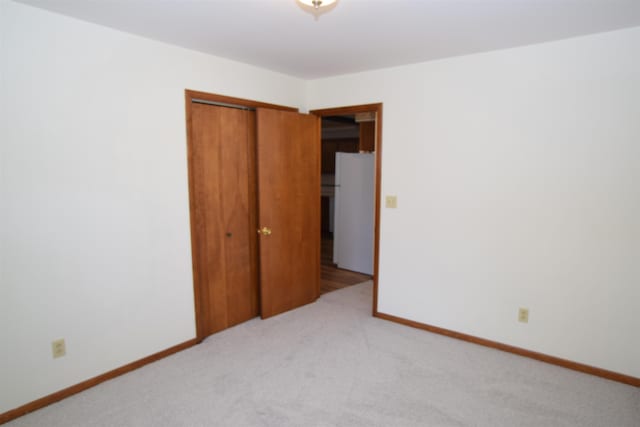 unfurnished bedroom featuring baseboards, freestanding refrigerator, a closet, and light carpet