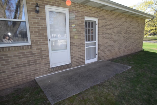 doorway to property featuring a yard and brick siding