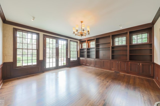 interior space featuring a chandelier, french doors, a wainscoted wall, dark wood-type flooring, and ornamental molding