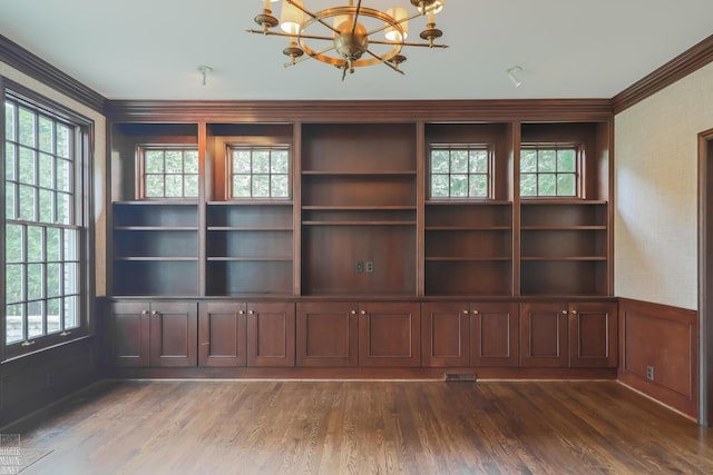 unfurnished room with dark wood-style floors, an inviting chandelier, ornamental molding, and a healthy amount of sunlight