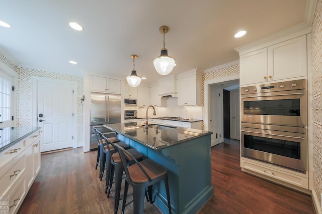 kitchen featuring built in appliances, a breakfast bar area, white cabinetry, a sink, and dark stone countertops