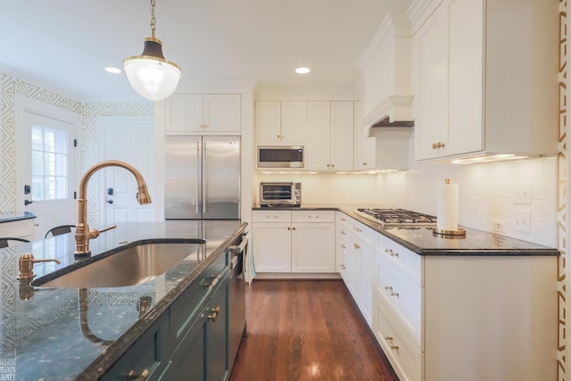 kitchen featuring pendant lighting, built in appliances, dark stone counters, white cabinetry, and a sink