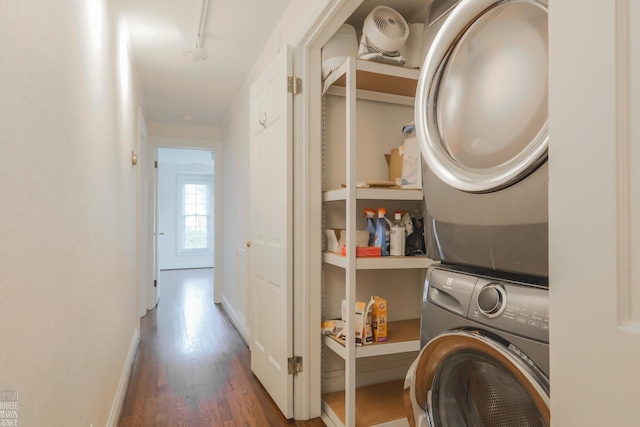 laundry room featuring stacked washer / drying machine, rail lighting, and wood finished floors