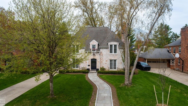 french country style house with concrete driveway, brick siding, an attached garage, and a front lawn