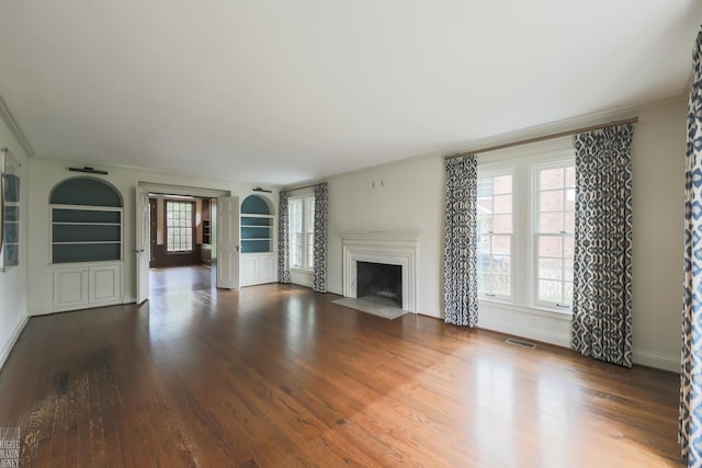 unfurnished living room with a fireplace with flush hearth, built in features, wood finished floors, and visible vents