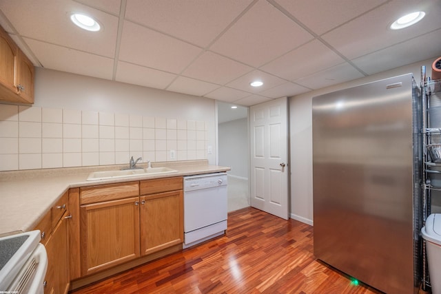 kitchen featuring white dishwasher, stove, wood finished floors, a sink, and freestanding refrigerator
