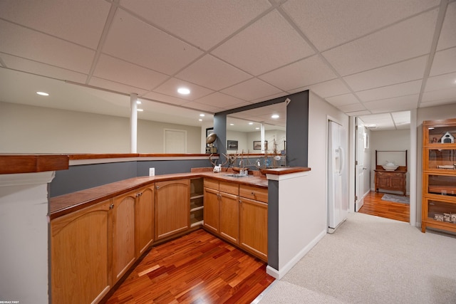 bar with indoor wet bar, a sink, a paneled ceiling, and light wood-type flooring