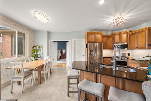 kitchen featuring a sink, appliances with stainless steel finishes, brown cabinetry, and a breakfast bar area