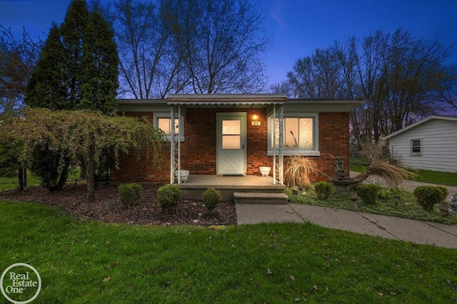 view of front of property featuring covered porch, brick siding, and a front yard
