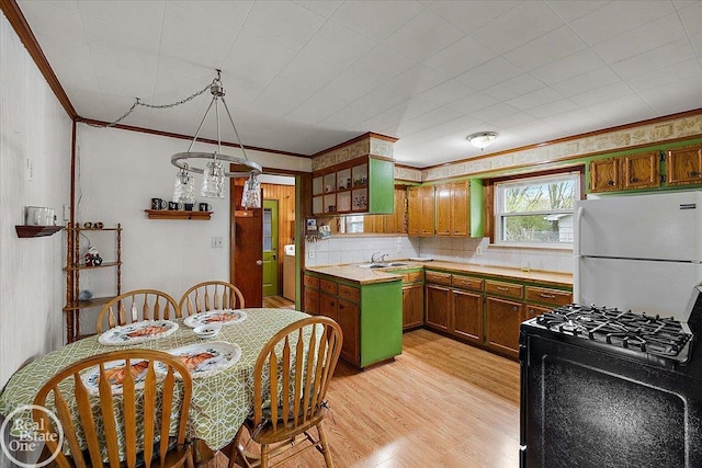 kitchen featuring open shelves, black gas range oven, light countertops, freestanding refrigerator, and light wood-type flooring