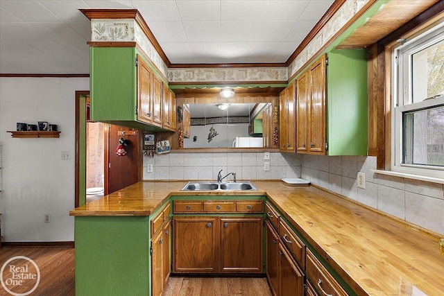 kitchen with a sink, wood finished floors, wooden counters, and ornamental molding