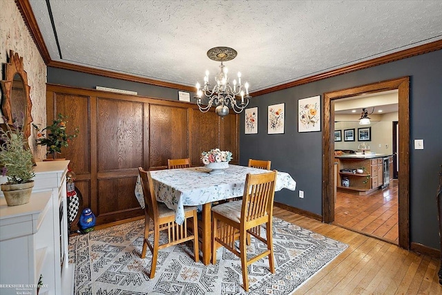 dining room with a textured ceiling, crown molding, light wood-type flooring, baseboards, and a chandelier