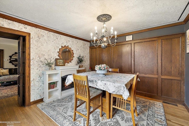 dining room featuring a textured ceiling, a chandelier, light wood-type flooring, visible vents, and ornamental molding