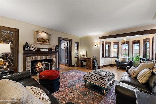 living area featuring a brick fireplace, baseboards, a chandelier, and wood finished floors