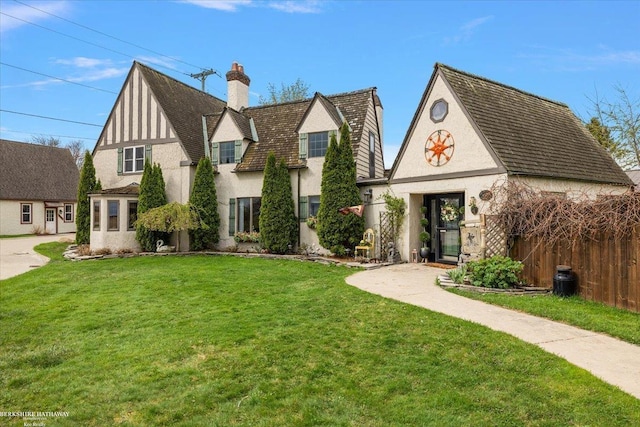 english style home featuring fence, a chimney, a front lawn, and stucco siding