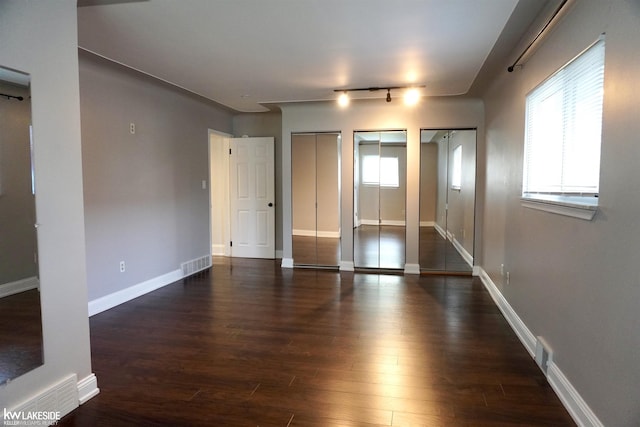 unfurnished bedroom with visible vents, two closets, and dark wood-style floors