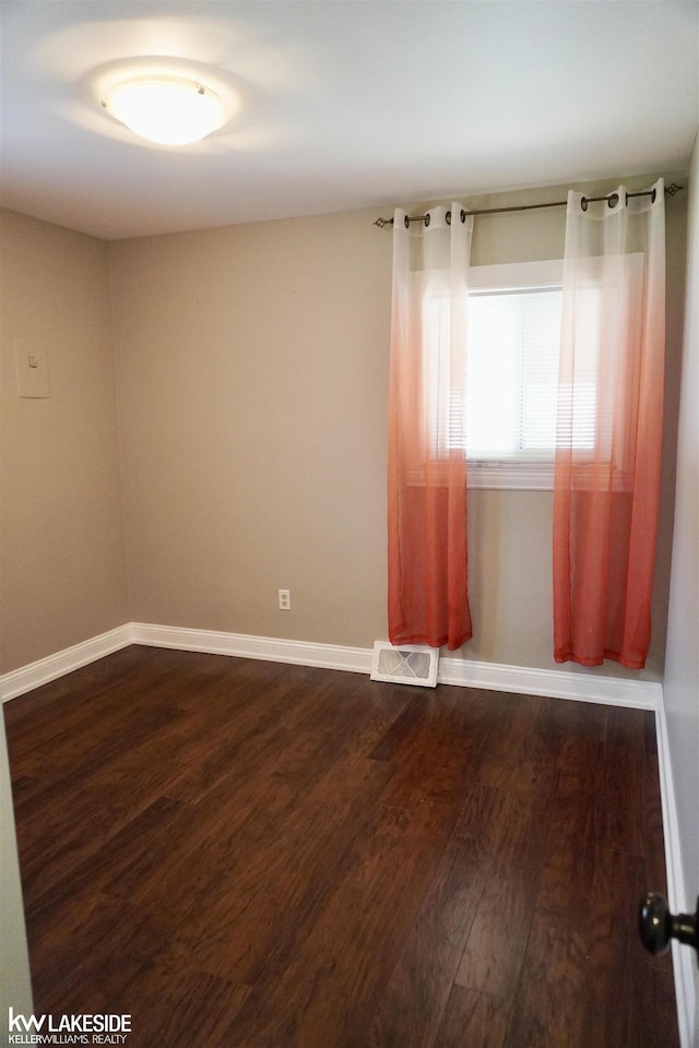 unfurnished room with baseboards, dark wood-style floors, and visible vents